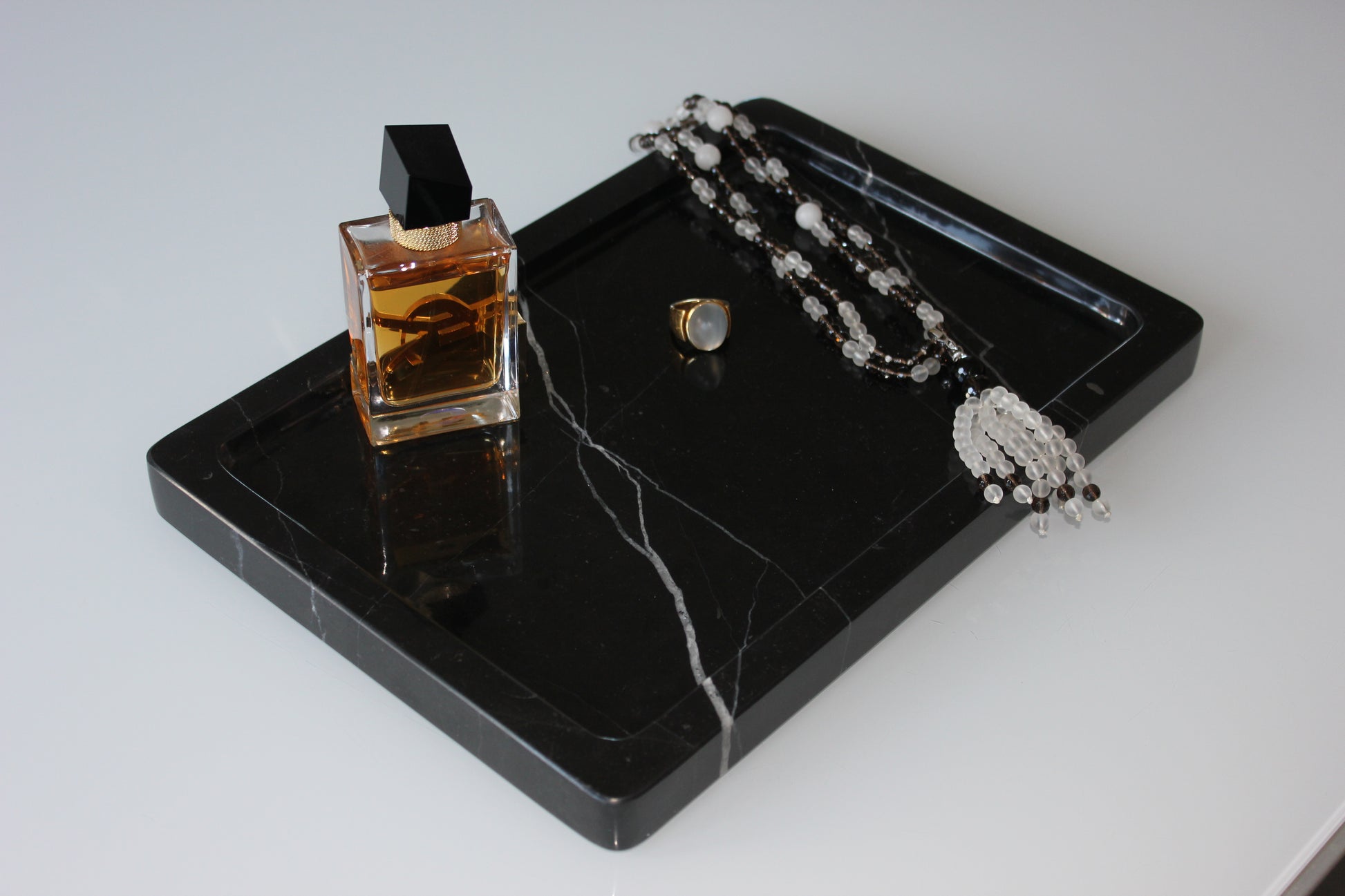 Close-up of perfume bottle, ring and necklace on polished Nero Marquina marble.