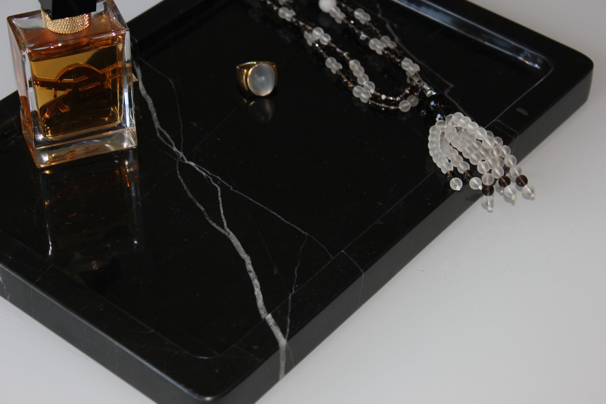 Luxury perfume, ring and necklace displayed on The Monolith tray in Nero Marquina marble.