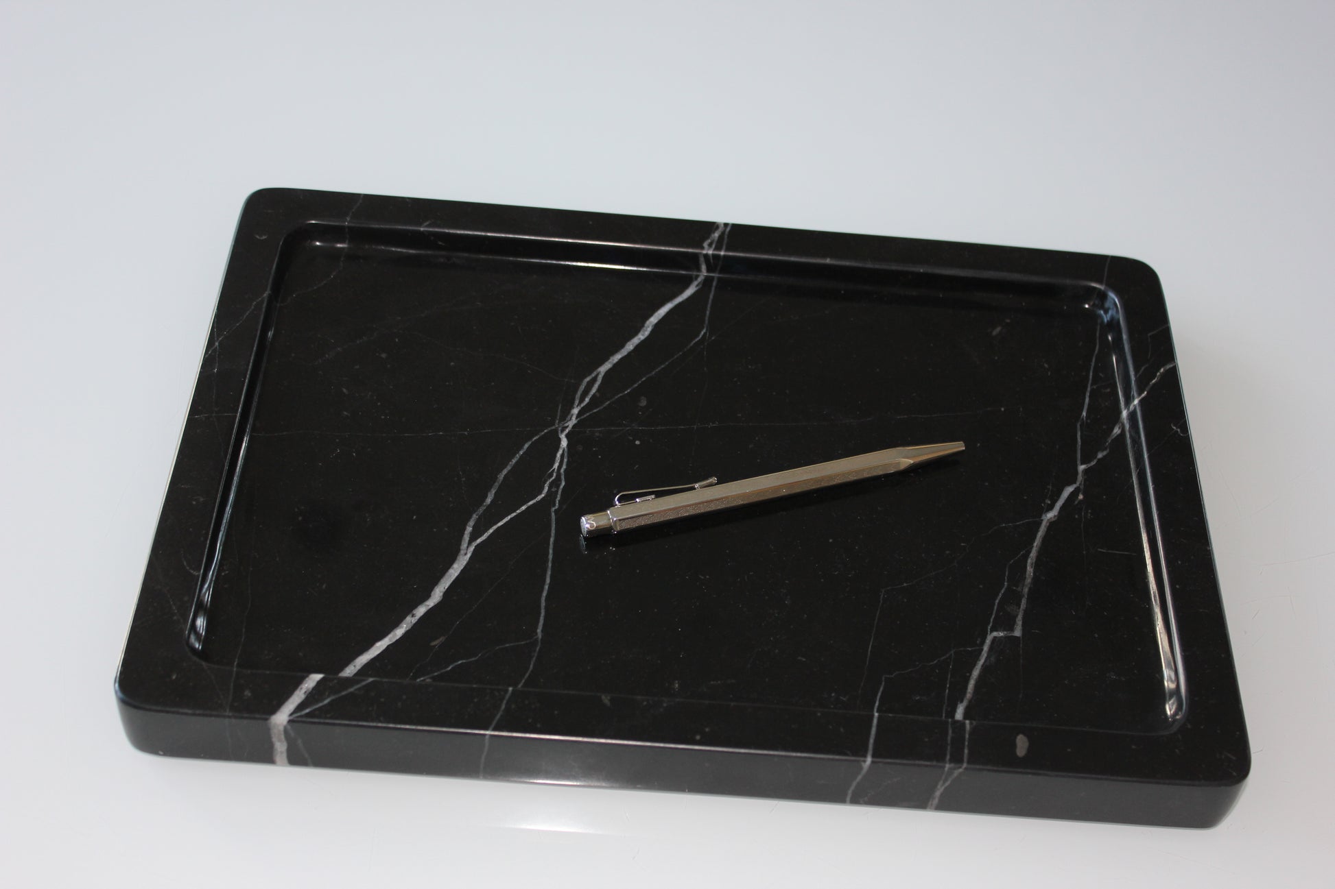 Minimal workspace with The Monolith tray in Nero Marquina marble and a silver pen.