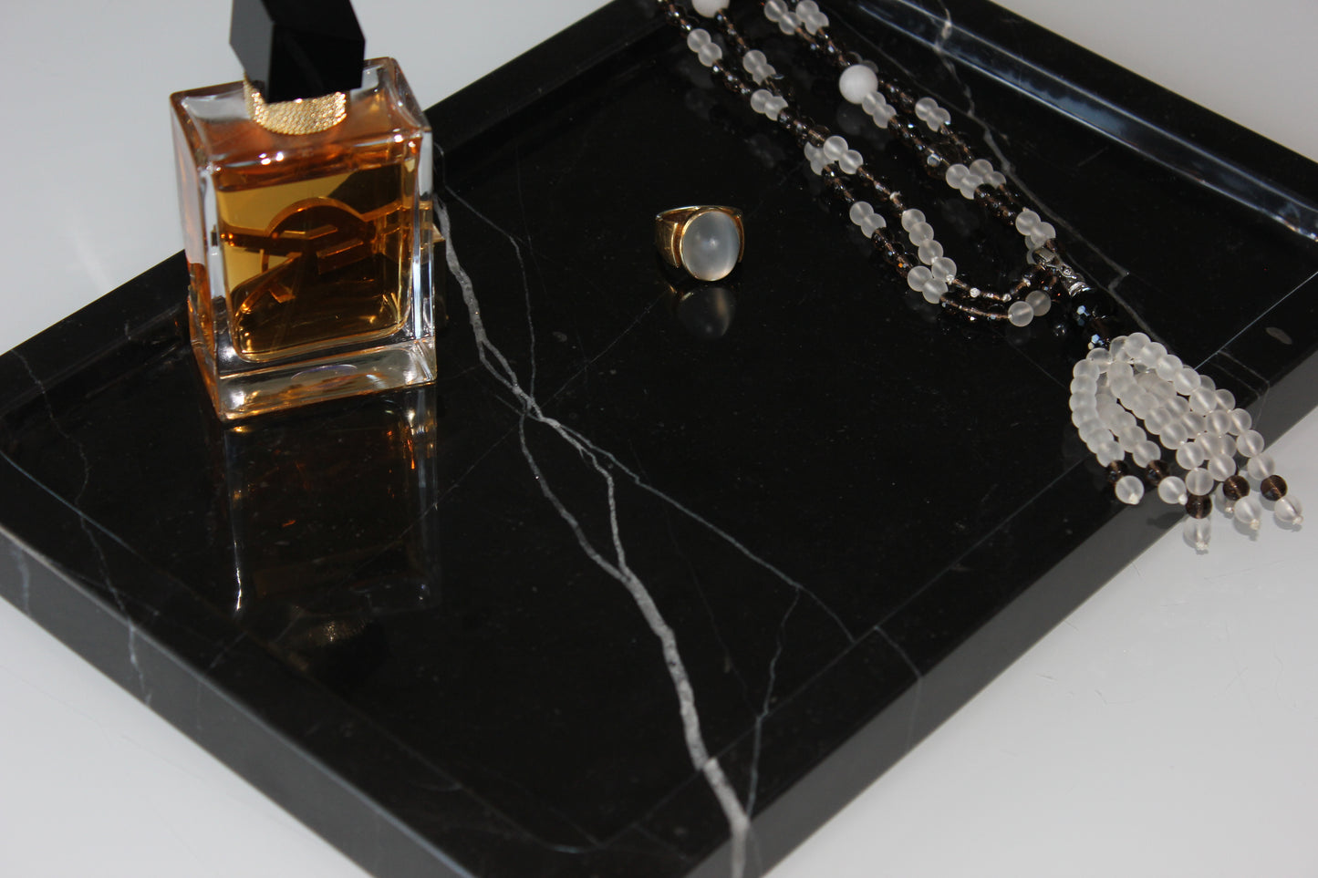 Close-up of perfume bottle, ring and necklace on polished Nero Marquina marble.