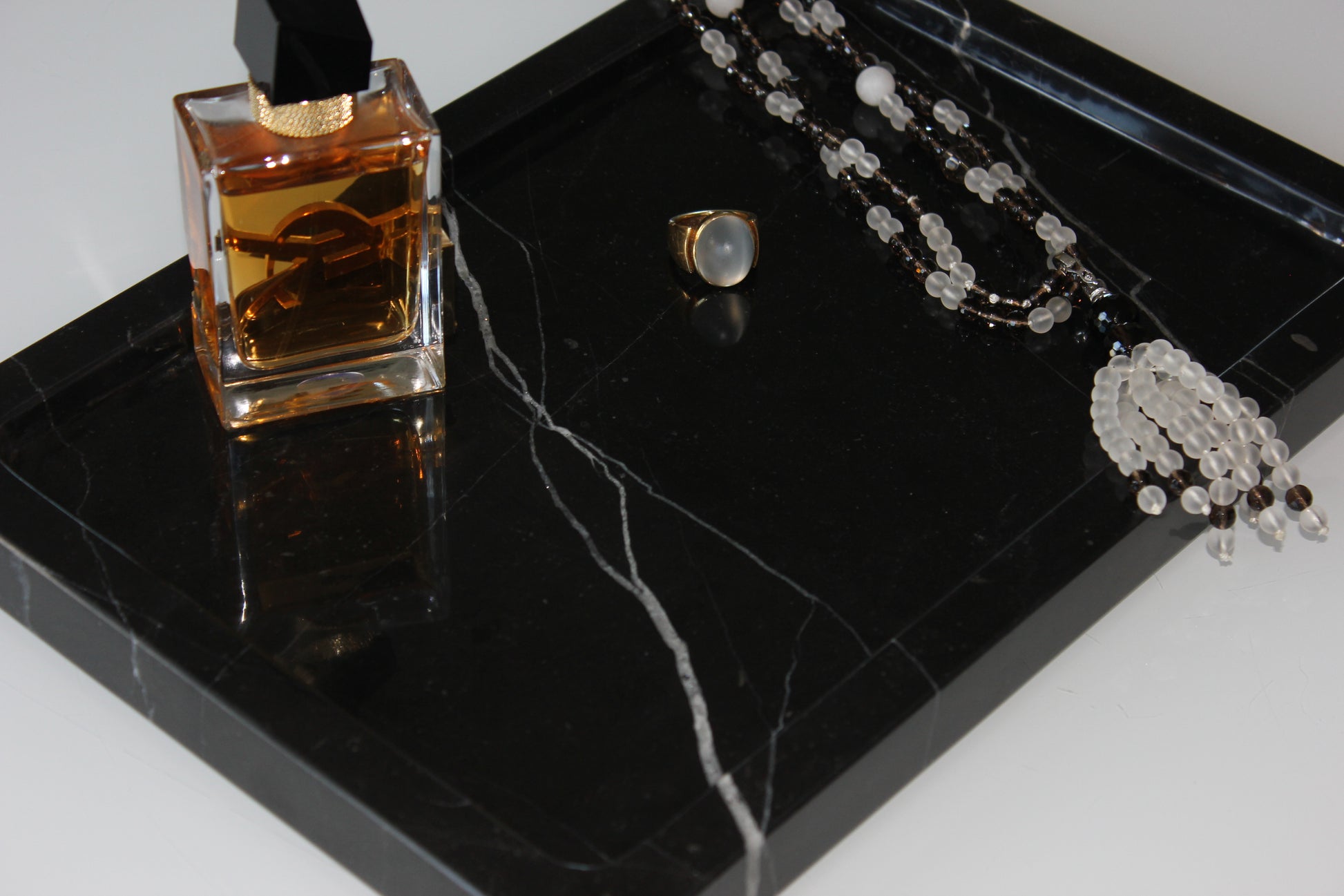 Close-up of perfume bottle, ring and necklace on polished Nero Marquina marble.